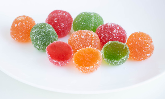 A pile of red, green and yellow jelly cubes on a white plate on a white background.