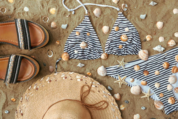 Summer shoes, straw hat and bikini set on beach sand Women's summer shoes, straw hat and stripped bikini set on beach sand among seashells and seafish swimwear bikini top bikini bikini bottom stock pictures, royalty-free photos & images