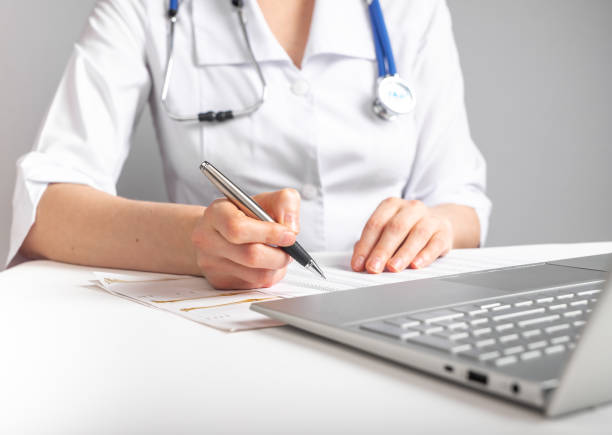 istock Doctor with stethoscope writing with pen about patient treatment or scheduling appointments. Woman in lab coat sitting at table with laptop. Health care and medicine concept 1396116684