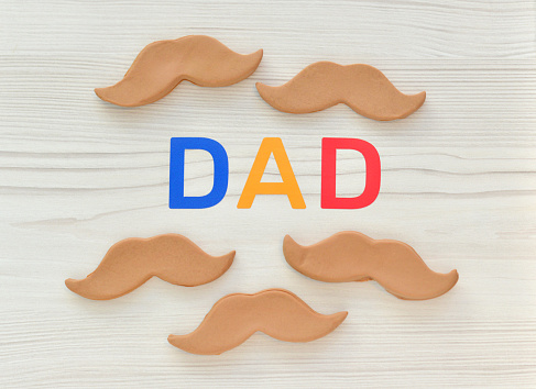 Closeup of homemade cookies in the shape of moustaches with text spelling out dad symbolizing a Father's Day gift.