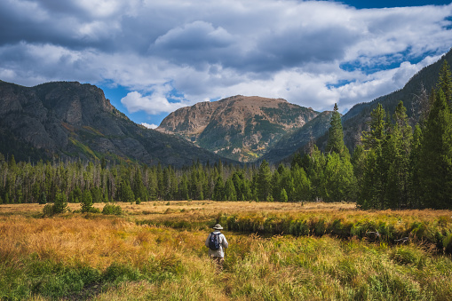 Beautiful view of meadow in Rocky Mountain National Park in autumn with small figure of man walking through; mountains in background