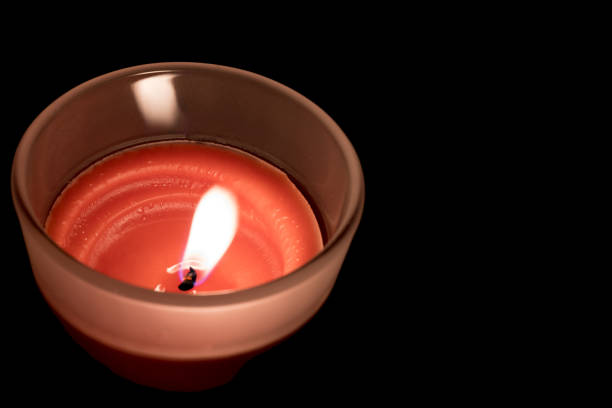 Close up of glass with burning red wax candle in it on dark background in moody mood as concept for mourning and condolences