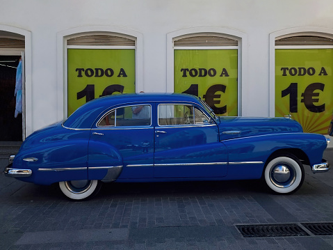 Elegant vintage blue car parked in front of signs with the text in Spanish 'todo a 1 euro' (everything at 1 euro)