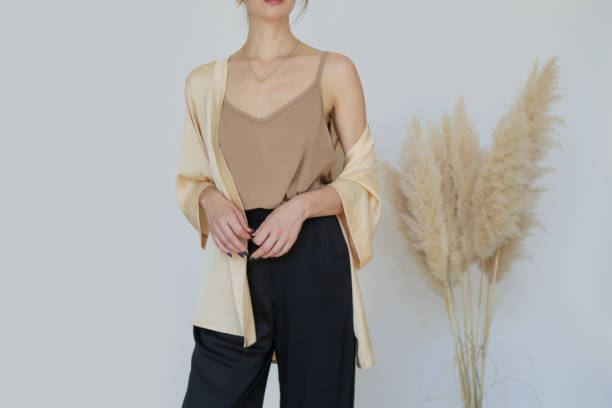 Female model wearing beige camisole cotton top and black trousers. Classic and simple summer fashion. Studio shot. Female model wearing beige camisole cotton top and black trousers. Classic and simple summer fashion. Studio shot. blouse stock pictures, royalty-free photos & images