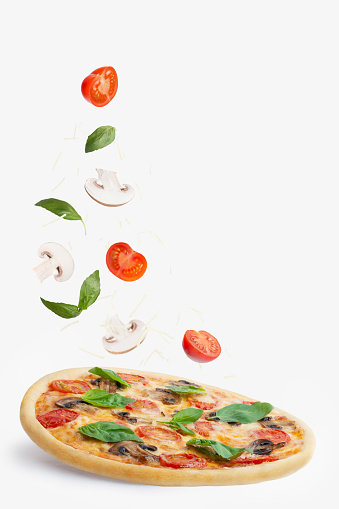 Pizza con champiñones, tomates, queso y albahaca sobre fondo blanco. Caída de ingredientes. Levitación photo