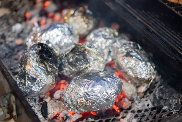 Baked potatoes with bacon, onions and baked vegetables in foil - tomatoes, eggplants, peppers on a gray wooden table.