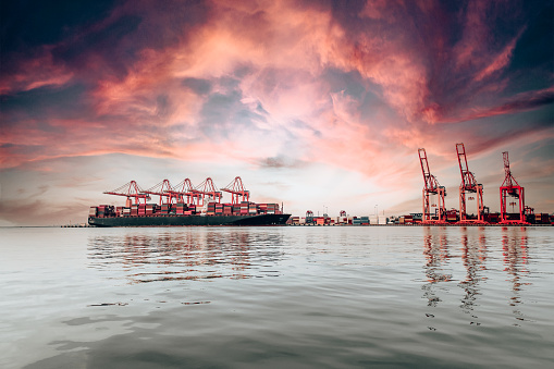 Cargo container ship moored at harbor. Loading or unloading containers with cranes.