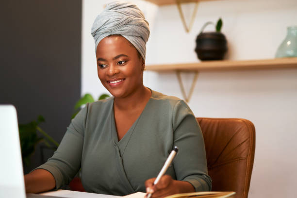 istock African american female freelancer smiling and making notes while working on her laptop. Woman writing and using computer while doing research or on a video call in her office 1396138029