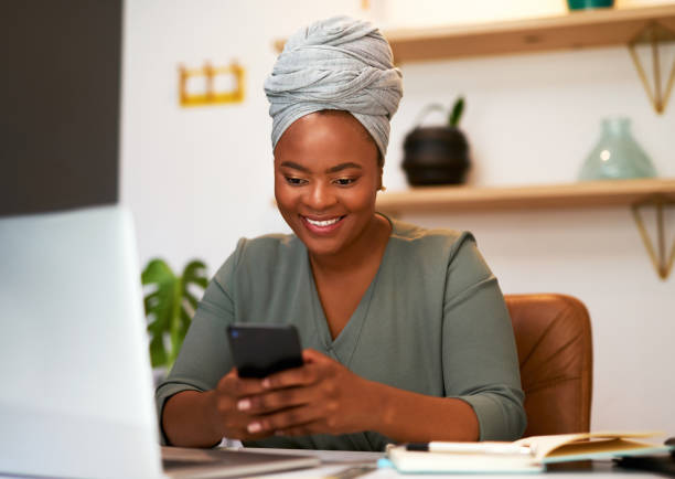 istock African business woman smiling while using smartphone in her office. Female entrepreneur smiling while sending or reading a text, surfing the internet or chatting on social network 1396138037