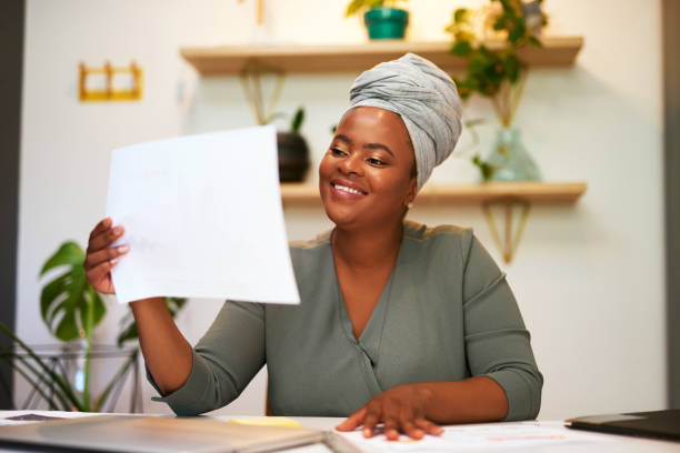 istock Smiling business woman looking satisfied while reading paperwork or document while sitting at her desk in a modern office. Female entrepreneur checking financial documents or statistics report. Looking satisfied with profit growth on project stats 1396138172