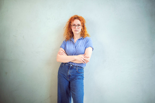 A woman in denim jeans is leaning against a white wall.