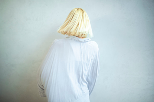 A view from the back of a blonde woman standing in front of a white background.