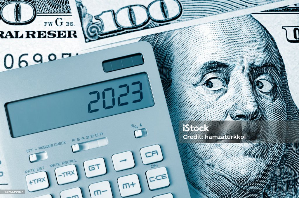 Ben Franklin's fear: 2023 2023. Benjamin Franklin looking calculator on One Hundred Dollar Bill. 2023 Stock Photo