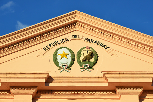 Asunción, Paraguay: double coat of arms of Paraguay, white circle with a golden five-pointed star surrounded an olive and palm branch, the reverse (here on the right) is also the Seal of the Supreme Court, it features a right facing golden lion with staff and liberty cap. About is the motto “Peace and justice” - pediment of the Cabildo, tympanum with block modillions - neo-classical building designed by the Basque architect Pascual Urdapilleta, built in 1844 for the executive and legislative branches, latter housed the National Congress - Plaza Independencia.
