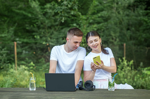 Man and woman in white t-shirts. Use laptop and smartphone for work and study. Summer season.