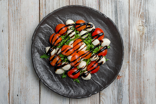 Salad with mozzarella, tomatoes and arugula with balsamic sauce on black plate top view on white wooden table