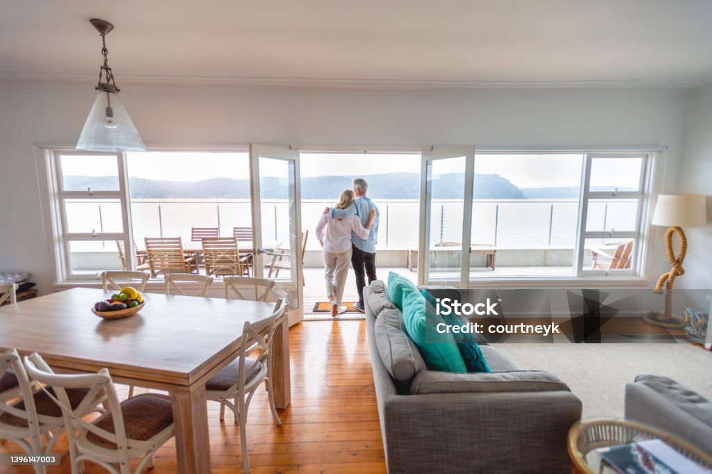 Mature couple looking at the view in their waterfront home. Mature couple looking at the view in their waterfront home. They look happy and contented. They are embracing. The ocean can be seen in the background. Senior Couple Stock Photo
