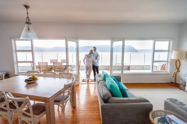 Mature couple looking at the view in their waterfront home. Mature couple looking at the view in their waterfront home. They look happy and contented. They are embracing. The ocean can be seen in the background. wealthy house stock pictures, royalty-free photos & images