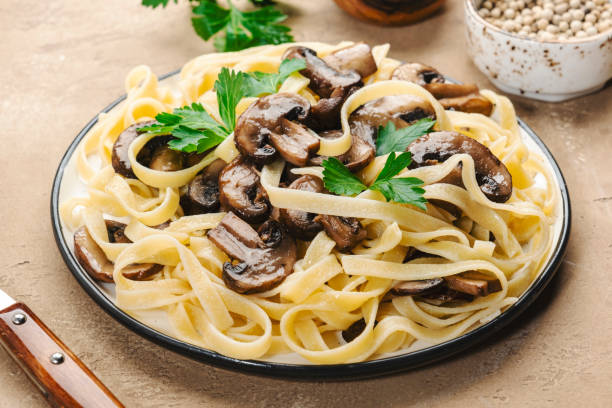 istock Delicious pasta with champignon mushrooms on plate with parsley on beige stone kitchen table background, top view. Healthy vegan cooking and eating. Italian food concept 1396148720