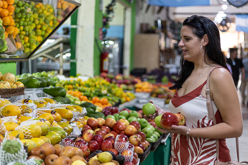 Black-haired woman choosing apples and pears at fruit stand