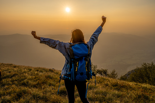 Back view of woman with raised hands standing above deep valley at sunset. Romantic view of landscape .Spending time in nature with friends, enjoying day in mountains.