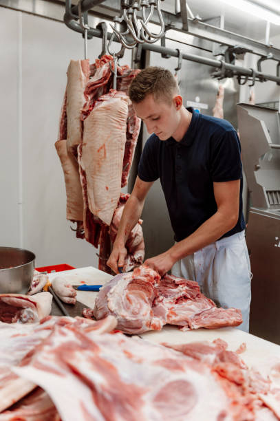 istock Young man apprentice at the butcher shop cutting meat 1396160911