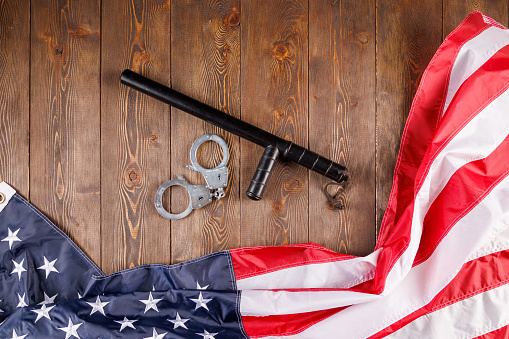 silver metal handcuffs and police nightstick near crumpled US flag on wooden surface