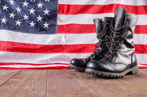 a pair of black police ankle boots stand in front of US flag on wooden surface.