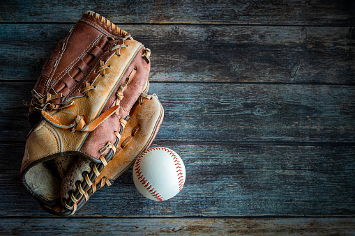 Leather baseball or softball glove with ball on rustic wooden background with copy space.