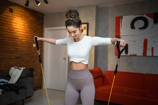 One woman beautiful female training at home in room using rubber resistance bands tubes sportswoman doing exercises alone health and fitness concept copy space