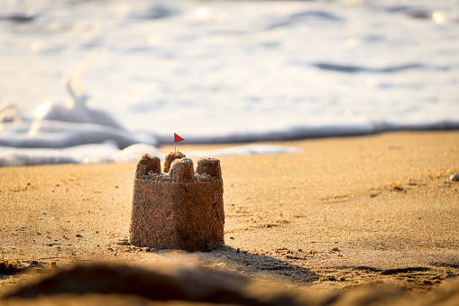 Sand castle with red flag on sandy beach in sea shore at sunset time , summer holiday vacation at tropical island.