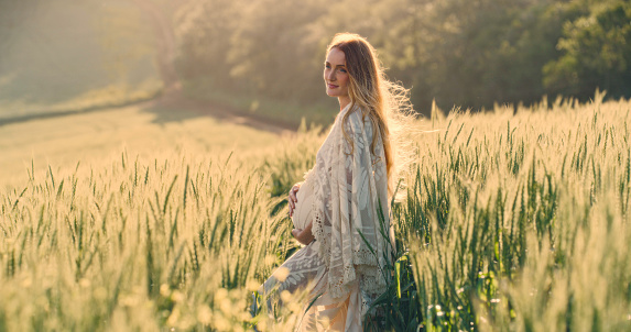 A beautiful pregnant young woman relaxing in a field in the countryside. Happy pregnant woman enjoying a relaxing maternity leave in nature
