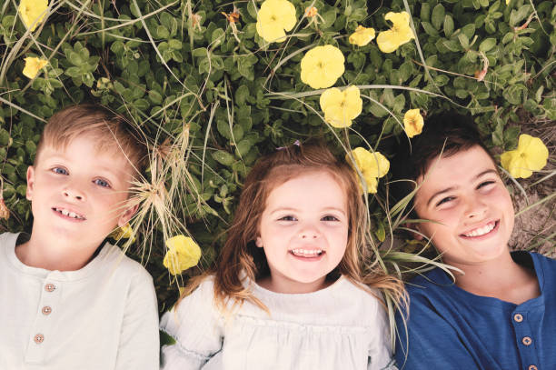 Three kids laying in the grass and flowers , looking at the camera and smiling