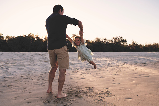 Father lifting little girl in the air and spinning around at the beach.