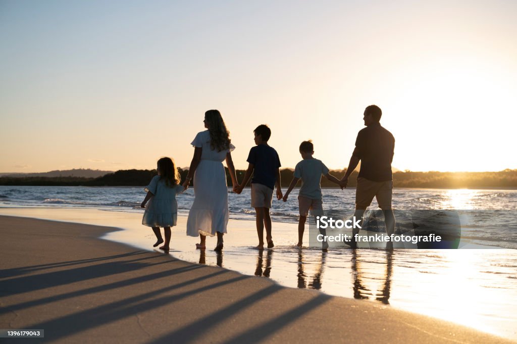 Family of five walking the beach Mother and Father with 3 kids holding hands walking along the waters edge with the sunset. Family Stock Photo