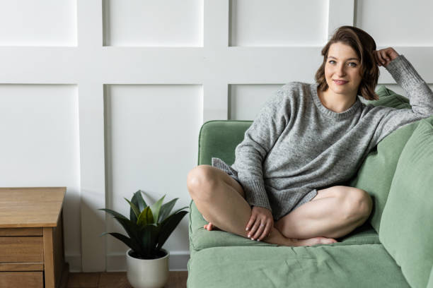 Beautiful young woman relaxed on the couch in the living room at home. Daylight. Female in a grey sweater filling comfortable at her house. Weekend Beautiful young woman relaxed on the couch in the living room at home. Daylight. Female in a grey sweater filling comfortable at her house. Weekend DOING NOTHENG stock pictures, royalty-free photos & images