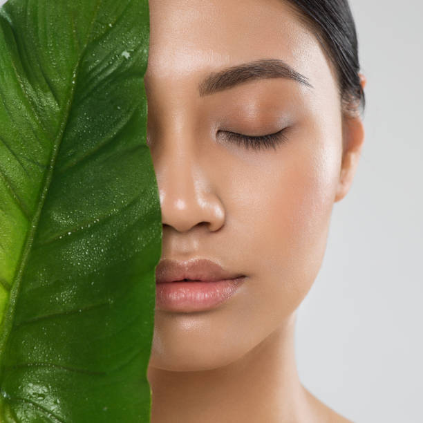 skin care. natural beauty woman. model with fresh clean skin make up and full lips with big green tropic leaf. eco cosmetics and spa cosmetology. asian girl close up portrait with closed eyes - leaf epidermis imagens e fotografias de stock