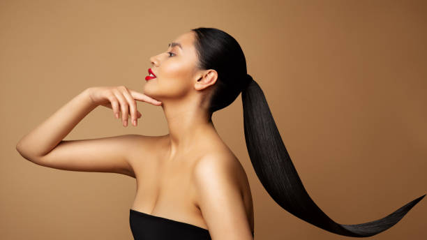 profil du modèle de beauté. jeune femme aux longs cheveux en queue de cheval. visage des femmes vue latérale sur fond beige. dame avec rouge à lèvres rouge et coiffure noire à queue droite - hairstyle fashion model make up fashion photos et images de collection