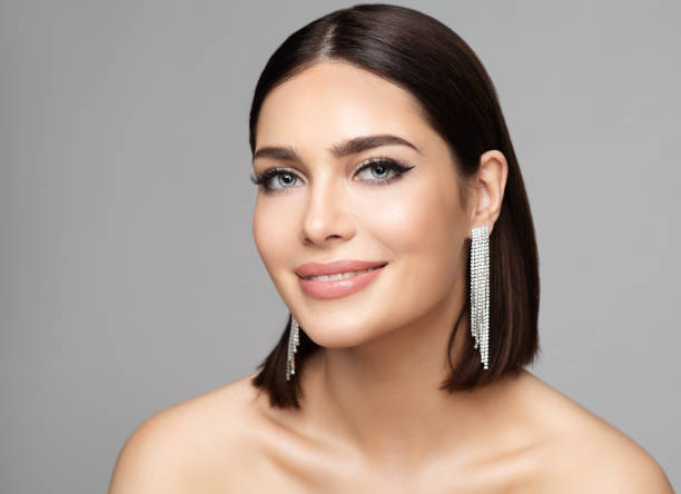 beauty woman portrait with perfect make up and silver earrings. smiling fashion model with bob haircut over gray. women full lips gloss makeup and diamond jewelry - full hair imagens e fotografias de stock