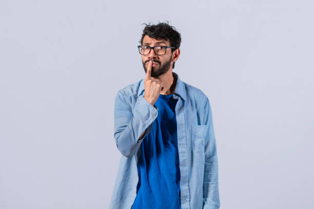 istock pensive young man with his finger on his lips on an isolated background, a pensive guy with a finger on his lips, pensive man on an isolated background 1396195054
