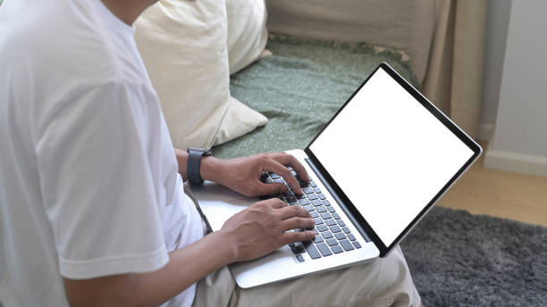 istock Cropped view young man in casual clothes using computer laptop on couch at home. 1396199636