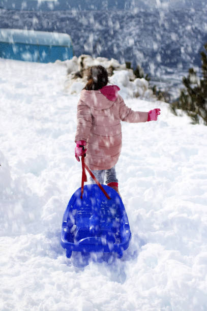Little girl is  pulling snow sledge on snowy mountain