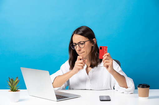 Hispanic pretty woman shopping online in front of laptop isolated on blue background.