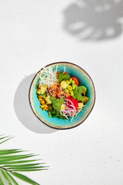 cuisine hawaïenne - poke bowl avec saumon, avocat, edamame et légumes. pokebowl dans un plat en céramique sur fond blanc avec des feuilles. menu d’été dans un style asiatique. aliments sains. - saladier photos et images de collection