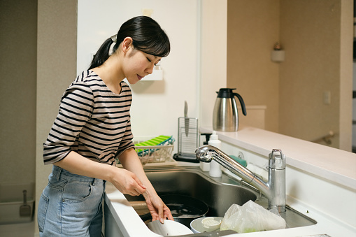 Asian woman washing dished in domestic kitchen
