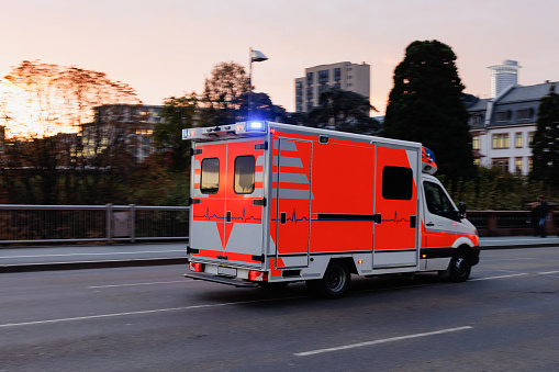 Red ambulance truck with emergency light driving over the bridge in Frankfurt am Main at dusk