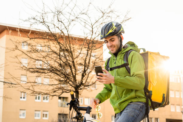 istock Smiling young man using bicycle to deliver boxes, documents and food at home, male courier using technology of smart devices to find address and sending work report 1396207330