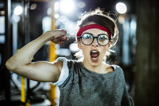 Portrait of a beautiful young woman flexing muscles while standing in front of a bright yellow background.