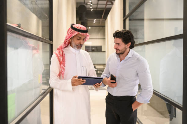 Saudi businessmen in 30s and 40s talking in office hallway stock photo