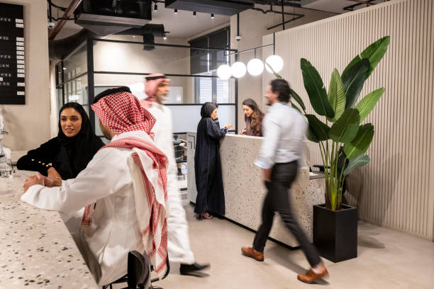Middle Eastern professionals in Riyadh coworking office Mixed-age business people in traditional Saudi and western attire relaxing at coffee bar, walking through lobby, and talking at reception desk. arabia photos stock pictures, royalty-free photos & images